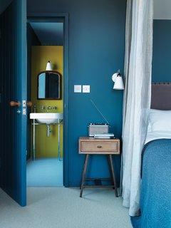 The bed and side table in the master bedroom are from Loaf. In the adjacent bathroom, an antique mirror hangs above a Duravit sink. "There’s a slight Arts and Crafts feel to it," says Marston of the house.