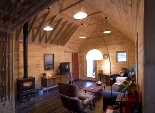 Inside the main living area, tongue-and-grooved white pine covers the walls and vaulted ceilings, and a red closet door, built of salvaged pine from the original house, slides along barn-track hardware. Image courtesy Chad Everhart Architect.