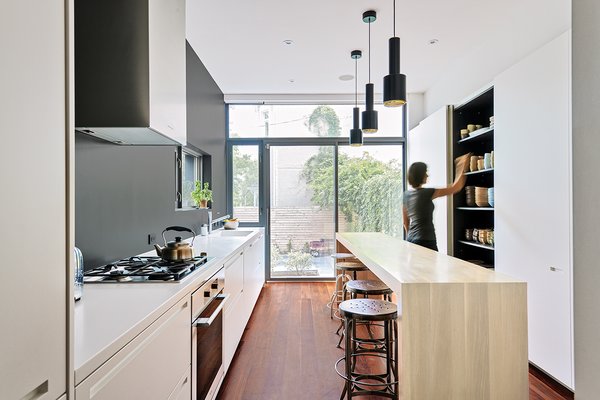The architects knocked out the kitchen’s back wall, where a single window had formerly let in a miniscule amount of light, and installed sliding glass doors instead. A soothing charcoal accent wall anchors the bright white cabinetry and Corian countertops, while pendant lights by Alvar Aalto hang above an oak island. The fixtures are from KWC, Dornbracht, and Catalano. Photo 3 of Contrast House modern home
