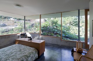In the master bedroom, stepped windows framed by Douglas fir mullions rest on low concrete walls that are flush with the easy-to-maintain, hand-troweled concrete floor. The platform bed is from Scan Design and the rattan chair is from Ikea.