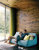 In the warm interior of the X House in Hennepin, Illinois, Diane Pascal and Thomas Richie enjoy the view from their boiled-wool Ligne Roset couch in the main living area, where wood paneling on the ceiling and walls mirrors the topography of the landscape. A gauzy green curtain adds a moment of color to the scheme. Photo 2 of New Grass Roots modern home