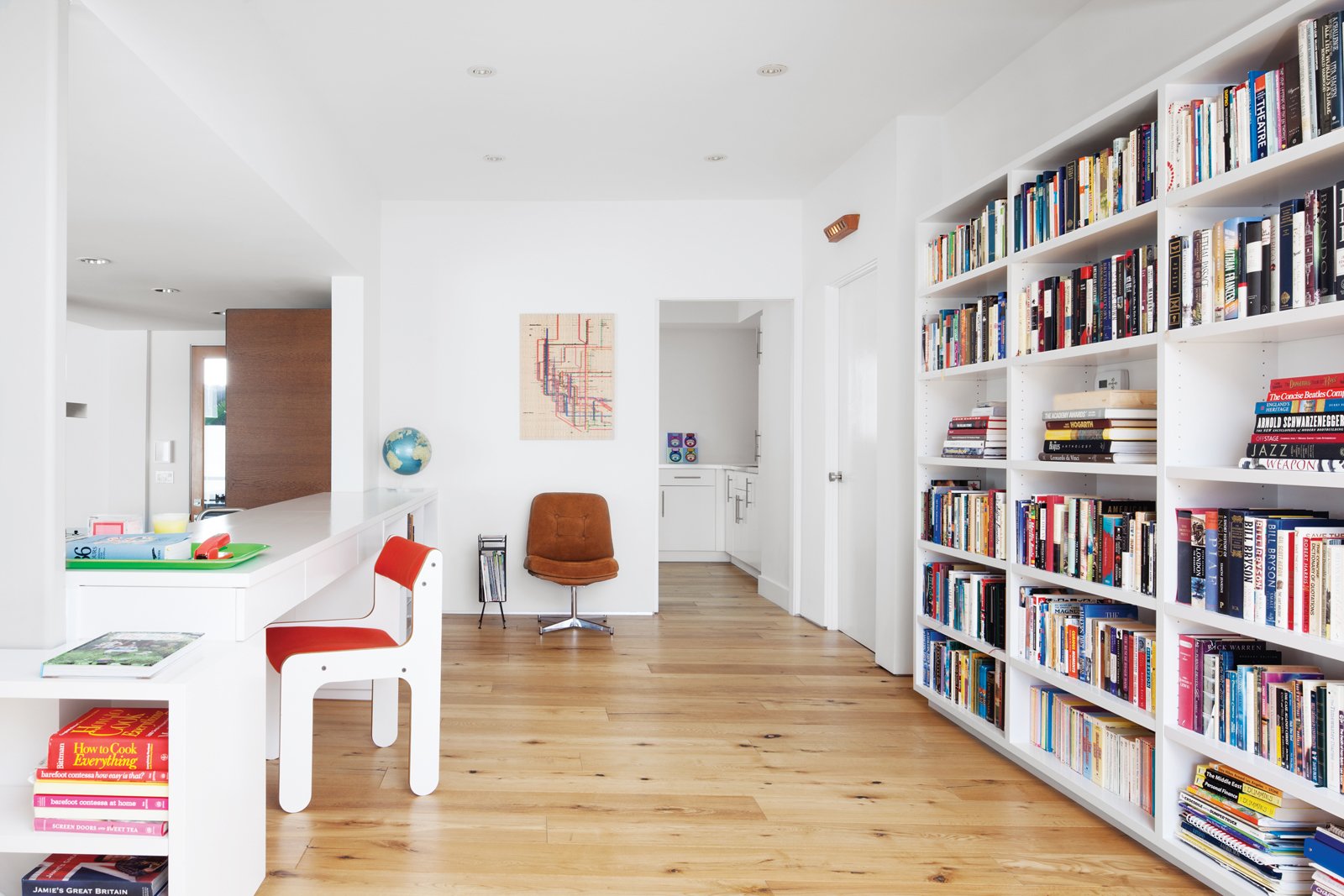 To impart a high-design feel to the space, Jacobs wrapped cabinetry from Ikea with a marble countertop and designed built-in bookshelves around the kitchen and study to help unify the area. Trips to shops in Palm Springs yielded the red side chair and metal magazine rack. The brown suede chair is from MidcenturyLA.