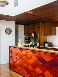 In the kitchen, Yuka makes baby Maude a snack at an island with original red tiles. Hanging cabinets were removed to maximize light and family-room views.