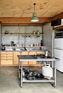 The designers fabricated everything in the house, down to the quarter-sawn pine and macrocarpa-wood kitchen cabinetry and concrete floor. "Physically the most challenging part of the build was wrestling an incredibly slippery concrete pump up the muddy driveway in the rain!" says designer Ben Mitchell-Anyon. The enamel pendant light is vintage. Photo by: Paul McCredie