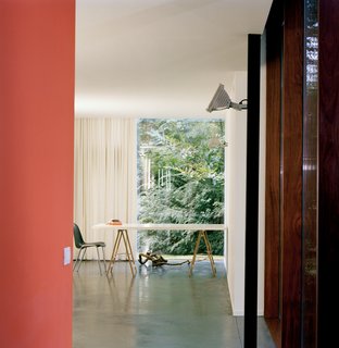 Van Everbroeck’s home office occupies the end of one arm of the building. An industrial outdoor light fixture is mounted on a black-painted steel post. The orange of the back wall was chosen to work with the glowing rays of the sunset and the silhouetted, dancing shadows of leaves.