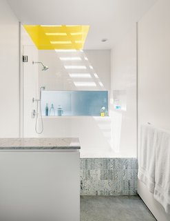 A Minimalist Duplex in Venice, California - Photo 8 of 9 - The master bathroom has a small window and a large skylight above the shower—and shares a translucent glass expanse with the kitchen, where it becomes the backsplash. "Even though it’s a buried room," Don says, "we have three sources of natural light. For the shower, we made a very high curb so you can stop up the drain and turn it into a big soaking tub. We used white, one-by-four-inch or one-by-six-inch Carrara marble tiles from Royal Stone and Tile. They come on a 12-by-12-inch sheet. I got the small tiles because you can use them to work the bottom plane into the shower." 