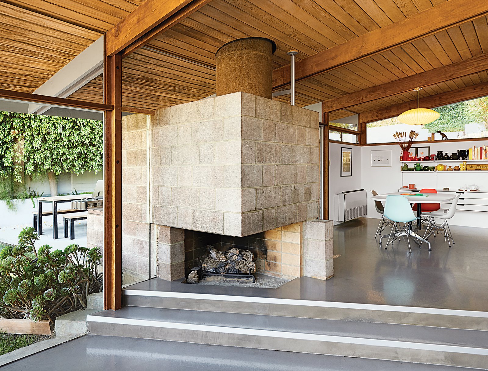 The dining area features a distinctive cinder block fireplace. Molded plastic side chairs are arranged around a Segmented Base table