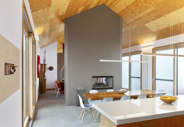 The home primarily features two materials: tile and wood. In between the dining room and living room, a fireplace is wrapped in floor tiles of a similar color to those lining the ground. Above, Douglas Fir plywood lines the ceiling. Rendely wanted a ceiling that had a rustic, distinctively non-urban look to it, and everyone agreed a wooden ceiling would make the space feel more cozy. Photo 3 of The Farm modern home
