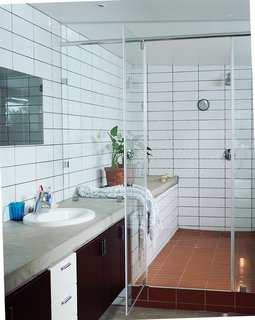 The shower-and-bath-in-one allows for the open feel of the house to translate within the bathroom. Simple concrete slabs function as countertops with inexpensive tiles laid floor to ceiling.