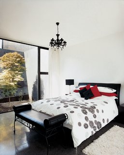 The decor of the master bedroom remains stark, but a black chandelier brings a touch <br><br>of complexity to an otherwise white space. The same maple tree can be seen through the rear glass wall, providing a visual focus for this wing of the house.