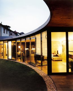 At night, the curved geometry of the house becomes even more clear. Lit from within, the house stands out against its backdrop of architecturally unexciting houses. Here, Johana and Tomáš look out onto an enclosed yard, a private space cut out of the bigger city.