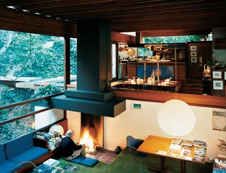 Ray sits at the central hearth on the north end of the comfortable sunken living area. From this perspective, you can see how the interior spaces flow into one another, passing one half-level up into the breakfast nook and kitchen and out from there onto the overgrown hillside. The various built-in furnishings have all been there since the house's construction.