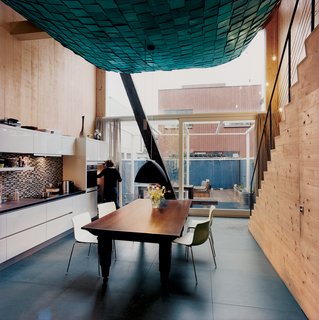 The suspended living room's scaly belly doesn't detract from the unfussy kitchen and dining area. A recycled Berlage-era table base (with a new tabletop), a deep blue lamp, and Arper chairs add to the maritime feel of the house.