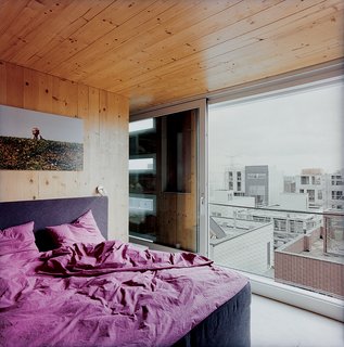 In the master bedroom, a large window looks out onto the surrounding rooftops.