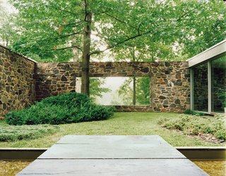 A large rectangular cut in the back wall of the house creates views from the entrance through a courtyard to the trees and lake beyond.