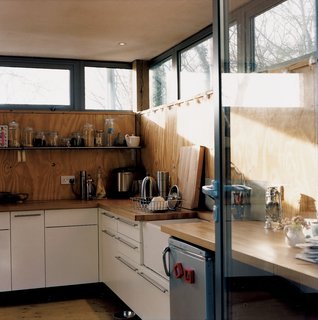 Beyond the kitchen is a secondary room that is a pantry, prep area, utility room, and entrance hall all in one. The standard beech-top counters from Howdens Joinery Co. are doubled up to achieve a three-inch thickness, with the rounded edges cut off.