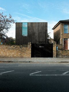 The facade achieves a notable sense of verticality for such a stout structure, with its stained-timber cladding aimed straight up toward the sky. The heavy, horizontal brick-work of the neighboring Georgian houses seems to imply aesthetic controversy, but in fact, during its short planning review, Reeve's house received letters of support from no fewer than five neighbors. The front gate opens onto a driveway, which in turn leads to a private patio around back.