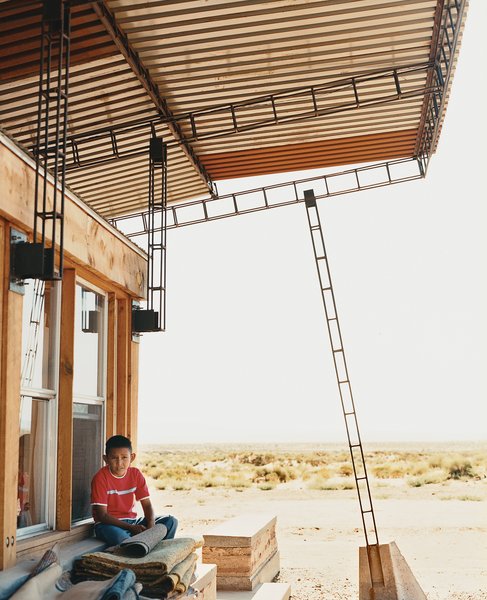 No Grid in Sight - Photo 3 of 8 - Nicholas sits in the shade of the roof; students cut and hand-welded thousands of reclaimed rebar pieces into a complex grid that would support four bi-level <br><br>corrugated-steel roof panels.