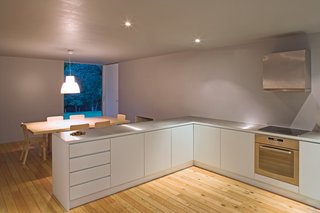 Vaz’s father’s restrained aesthetic is carried in the interior design scheme, which is reserved to the point of being austere. The light-colored, knotted wood provides a desirable warmth to the sparsely decorated space, which doesn’t in any way aim to compete with the outdoor scenery. Portuguese designer Álvaro Siza’s Lorosae pendant lamp bathes the simply furnished kitchen in warm light.