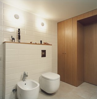 Palace Intrigue - Photo 4 of 13 - In the bathroom, which is tucked under the mezzanine, the toilet-bidet set from Pozzi Ginori boasts rounded rectangles with pleasingly deep but minimal basins. The wall sconces are from the Spanish lighting company Vibia, and fit neatly between brick-like rectangular tiles.