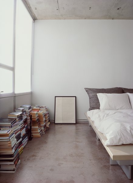 Who needs shelves when there's plenty of floor space? Stacks of books and a framed print sit alongside a Peter Maly Ligne Roset bed, reupholstered in stiff linen.