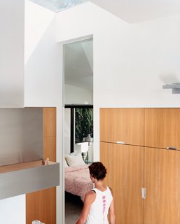 Dawn Farmer walks from the kitchen to a guest bedroom. The seven-foot-tall doorway lines up with the glass doors and cabinetry throughout the house—which is made of <br><br>13-layer multi-ply apple core with rift-oak veneer.