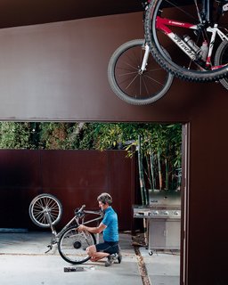 Pierre Kozely mends his bike on a patio in the rear yard, seen from their garage—which was transformed into a media room. Behind him is a Cor-Ten rolling gate that gives access <br><br>to the back alley.