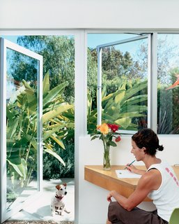 Dawn Farmer sits at her desk made of multi-ply apple core with rift-oak veneer, manufactured by Pietrarte. The garden is planted with lavender, red ginger, flax, and California pepper trees.