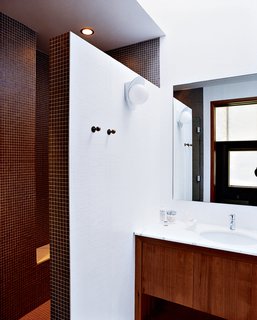 A double-size shower, clad floor-to-ceiling in tiny earth-toned tiles, was built after relocating the water heater and claiming its space. A chic yet discreet toilet is wall-hung and the tank concealed, greatly ameliorating the somewhat claustrophobic feel of the original bathroom.