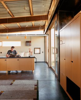 Architect Eric Logan sits in the guest house on his property. The interiors are made up of oiled masonite wall paneling, raw MDF cabinetry, and an oiled concrete floor.