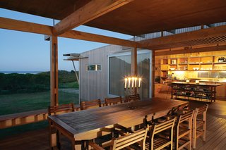 The outdoor room is backed by a gabion wall made of stone. Rainwater runs off the roofs into a channel before being funneled through pipes concealed within it to an underground concrete tank.