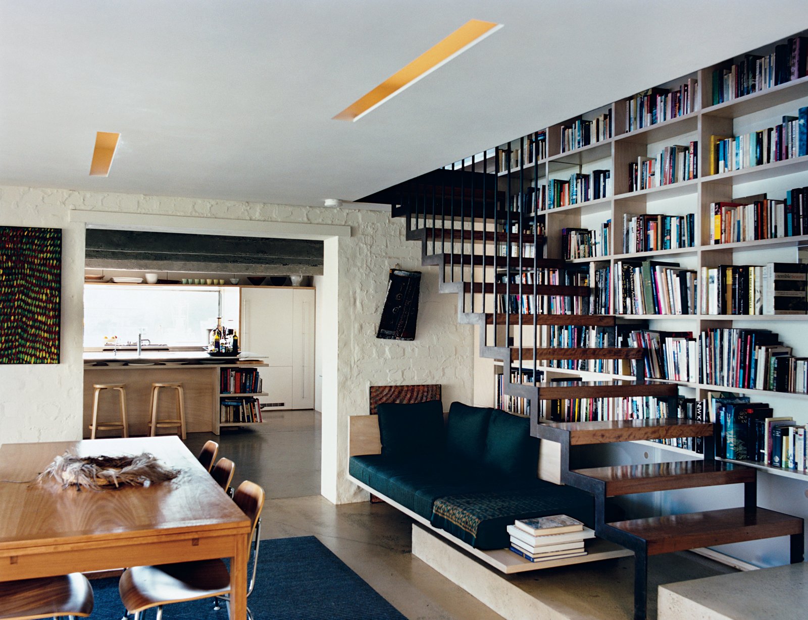 Inside, a suspended staircase rises up past the couple’s bookcase over a well-lit seating nook. Aalto stools by Artek join Eames molded plywood dining chairs by Herman Miller to give an especially modern touch to the kitchen.