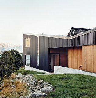 The home is mostly clad in black trapezoidal-profile steel, with cedar boards lining what the owners call the "human spaces"—external passages between buildings. A solar hot water system perches on the roof.
