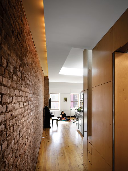 Although the apartment’s only windows are on the far ends of the space, skylights keep things bright. Recessed lighting along the brick wall supplements the daylight.