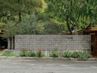 A wall of burnished concrete block protectively isolates their indoor and outdoor living areas from the busy road.