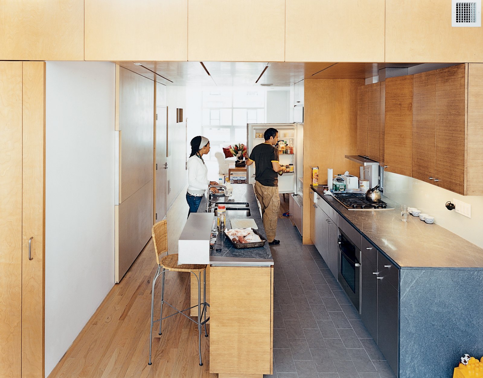 In the kitchen, the architects contrasted the oak floor, bamboo cabinetry, and birch walls and ceiling with what architect Jonathan Knowles calls “a family of grays”: granite floor tiles, limestone countertops, and the steel stairway. The birch wall behind Yvette is actually the sliding door to the pantry closet.