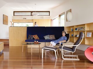 Hannah Ferguson relaxes in her living room. Her daughter Joanna prepares dinner in the open kitchen, behind and above the plywood banquette designed by the architects.