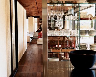 The ever-important Italian kitchen pours out through glass walls into the living room and onto the porch. A group of benches allows guests to hang out, drink wine, and pester the chef, while stainless-steel basins on rollers underneath give hungry kids easy access to snacks. Stainless-steel-and-glass shelving by the architects provides open storage for plates and glassware.