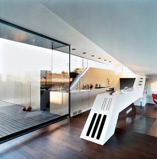 The "culinary cockpit" (a.k.a. the kitchen) stands at the center of the apartment on a raised platform. A long, white slanted counter contains hi-fi speakers and a BUS-system panel of 18 buttons for controlling lights, curtains, heating, ventilation, etc.