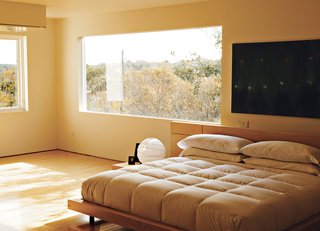Home Cooking - Photo 4 of 8 - In the third-floor bedroom, horizontal wood-framed casement windows by Pella open out to tree-filled views of Lake Austin and Westlake Hills. Comfortably austere, the only furniture here is the bed, two nightstands, and a marble table for books and candles. Erik designed the bed, nightstands, and marble table; the paintings are by Jair.