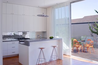 Noe Valley Renovation - Photo 11 of 17 - Grist and Goldberg wanted an open kitchen so their guests could gather around a beautiful space without feeling cramped in a tiny room. Goldberg instantly fell in love with an Ann Sacks glass tile backsplash that Samaha and Hart showed the couple during the design process, but she wasn't willing to spend $100 per square foot on the product. Instead, Goldberg had their contractor make three panels of cement board that would fit in the backsplash space and she and a friend spent their evenings gluing on glass tiles that she purchased online. When they finished, the contractor came back, installed the panels, and Goldberg filled in the gaps. Outside, chairs from Ikea and an Inox table from DWR provide a space to sit on the deck.<br><br>Photo by <br><br>Sharon Risedorph