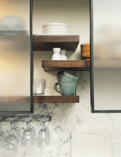 The Feld kitchen bridges eras by bringing together traditional designs and materials (the big Shaw’s Original English farmhouse sink, fir floors, honed marble counters) with industrial designs. Open walnut shelving helps convey a sense of lightness. The pot-and-pan drawers pull out for easy access, while rolling steel-framed panels of textured glass above the counter act as a scrim, allowing the Felds to choose what to obscure and what to display.