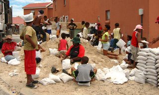 Luyanda Mpahlwa - Photo 3 of 9 - Mpahlwa took inspiration from the vernacular architecture of his youth in a rural part of the Eastern Cape, where people built homes from mud, water, and timber, to transform what is generally considered a nuisance—the abundance of sand—into an invaluable resource for holding down a house. Members of the community, seen here, gathered together to pack bags full of sand. Image courtesy Interactive Africa/ Design Indaba