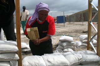 Luyanda Mpahlwa - Photo 4 of 9 - Once the frame of the house was constructed, the townspeople filled the wall space with sandbags. Here, Olga Jonkers uses a handmade tool to compact the bags that will become the walls of her future home. Image courtesy Interactive Africa/ Design Indaba