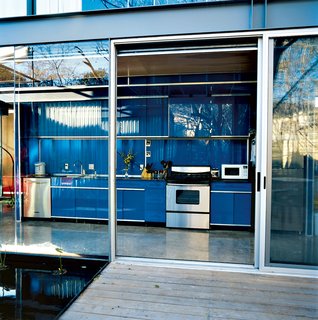 The minimal aesthetic is seen in the galley-style kitchen, where the cabinets have no visible hinges or knobs. The stainless steel appliances are by KitchenAid.