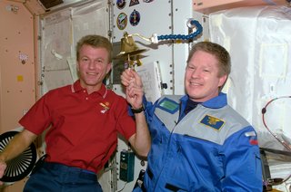 Astronauts Brent W. Jett, Jr. (left) and William M. Shepherd participate in an old Navy tradition of ringing a bell to announce the arrival or departure of someone to a ship. The bell is mounted on the wall in the Unity node of the ISS. The bell-ringing took place shortly after an in-space reunion on STS-97 Flight Day 9. Photo taken December 8, 2000. Image courtesy of NASA.