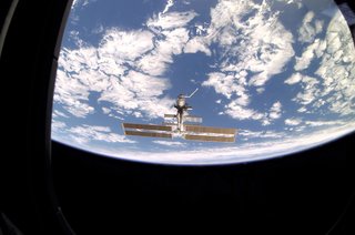 As seen through a window on Endeavour's aft flight deck, the ISS, then staffed with its fourth three-person crew, is contrasted against Earth's horizon during a farewell look from the shuttle following undocking. Photo taken December 15, 2001. Image courtesy of NASA.