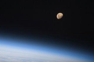 A gibbous moon is visible above Earth's atmosphere, photographed by an STS-128 crew member on the Space Shuttle Discovery during flight day three activities. Photo taken August 30, 2009. Image courtesy of NASA.