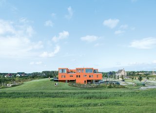 Seen here from the south, Villa van Vijven’s orange facade is meant to mimic the tiled rooftops of Holland’s country buildings, while the building’s horizontal pull echoes the flat landscape. The second-floor living rooms look out on the 4,200-square-foot communal garden, one of only two shared spaces in the whole community. Bob Krone, Koos Sweringa, and Marianne Schram stroll the grounds.