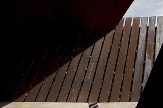 Rocks and earth are visible between the steel blades as visitors walk down the path. In the dark lower areas of the structure, daylight creeps in through cracks between earth and steel.